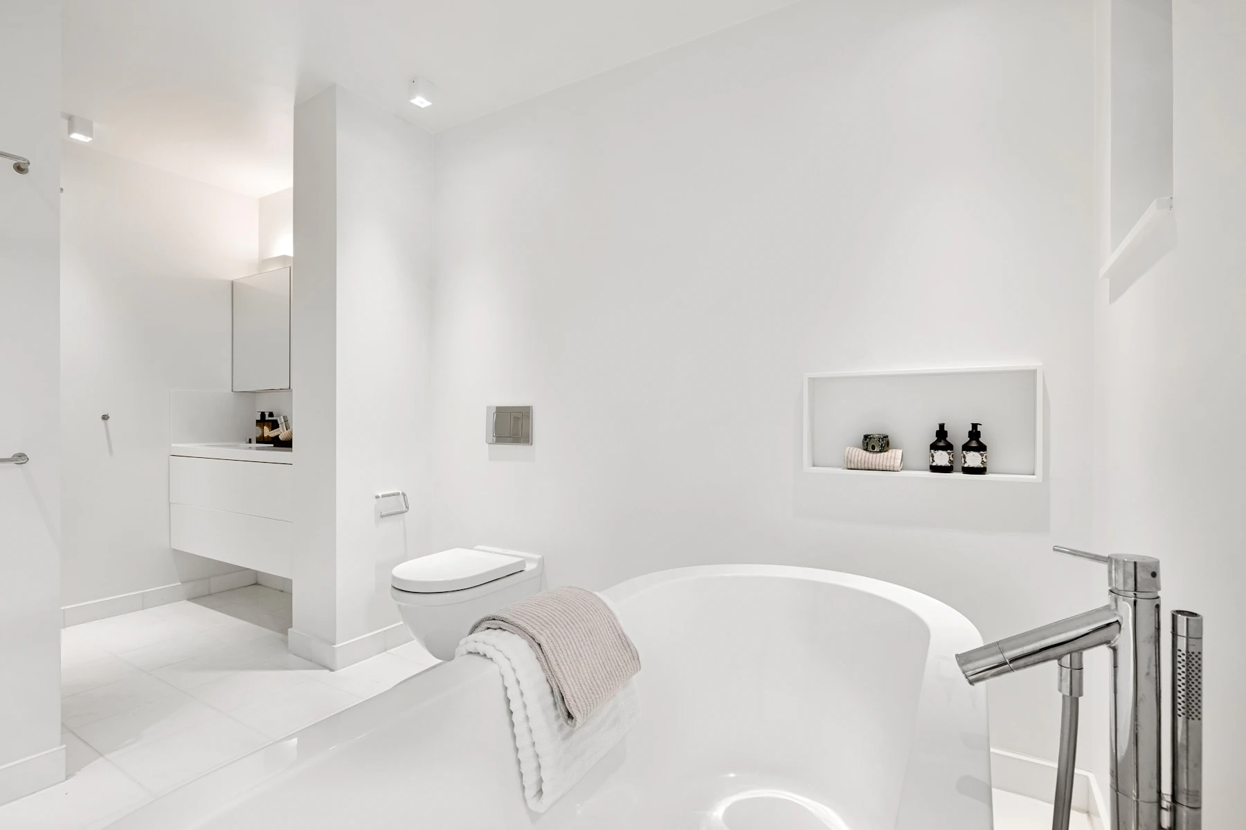 Une salle de bain blanche et claire avec une grande baignoire et un lavabo, lumière douce