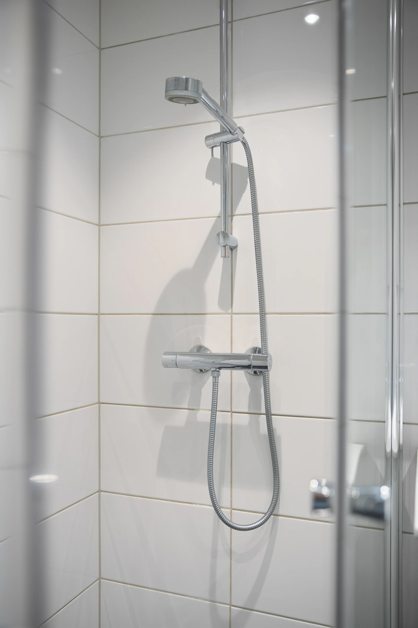 Chrome showerhead, handheld shower and thermostatic control mounted on white tiled walls inside a shower enclosure.