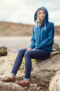 A woman sitting on a rock wearing a blue hoodie