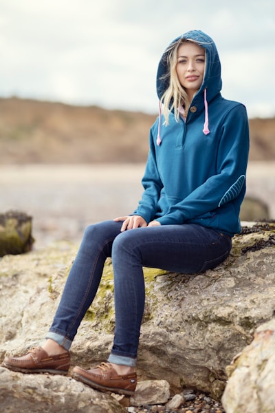 A woman sitting on a rock wearing a blue hoodie