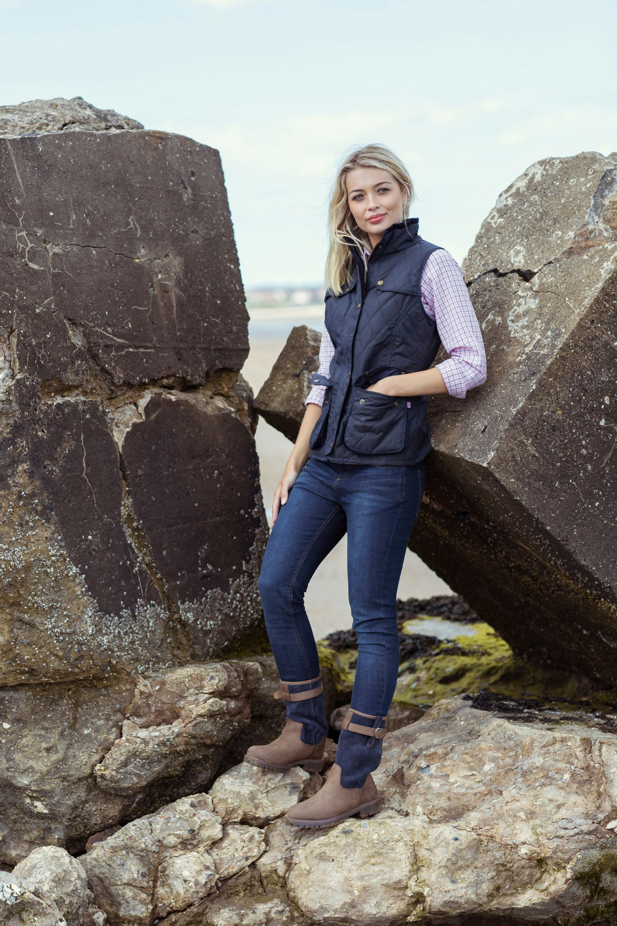 Une femme debout à côté de gros rochers sur une plage