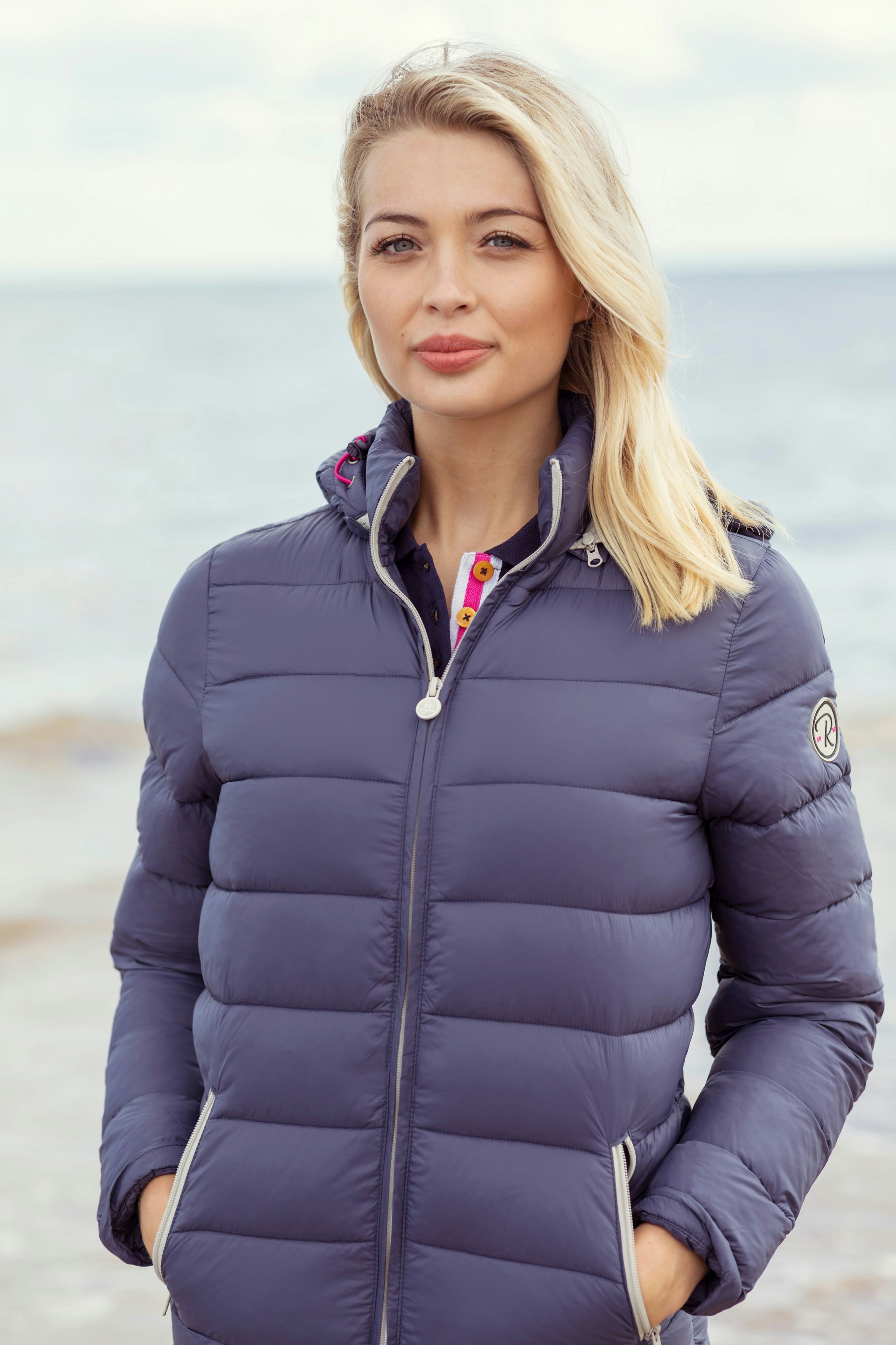 A woman standing on a beach wearing a blue jacket
