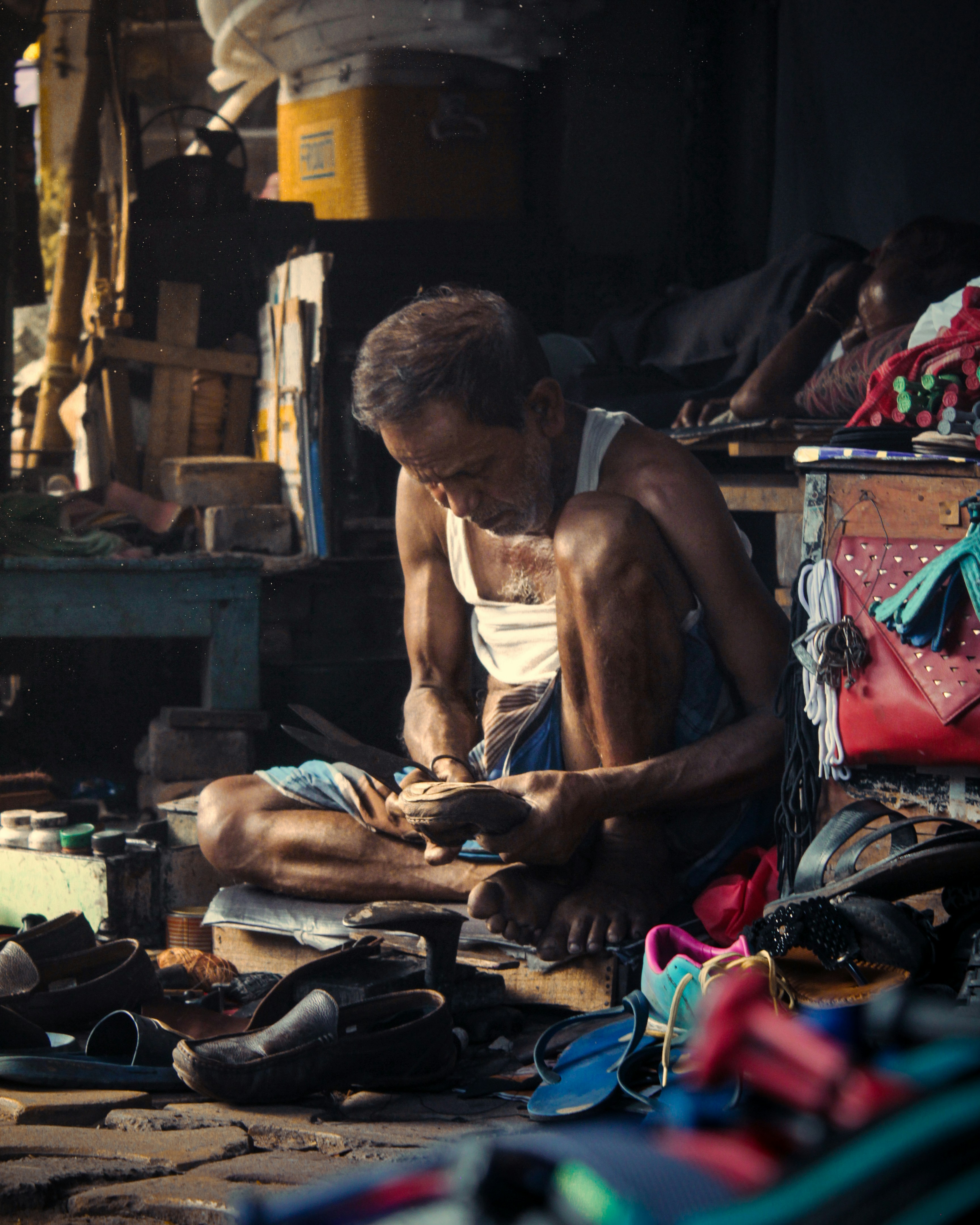 A man sitting on the ground in front of a pile of shoes