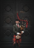 A man in a kilt holding a teddy bear