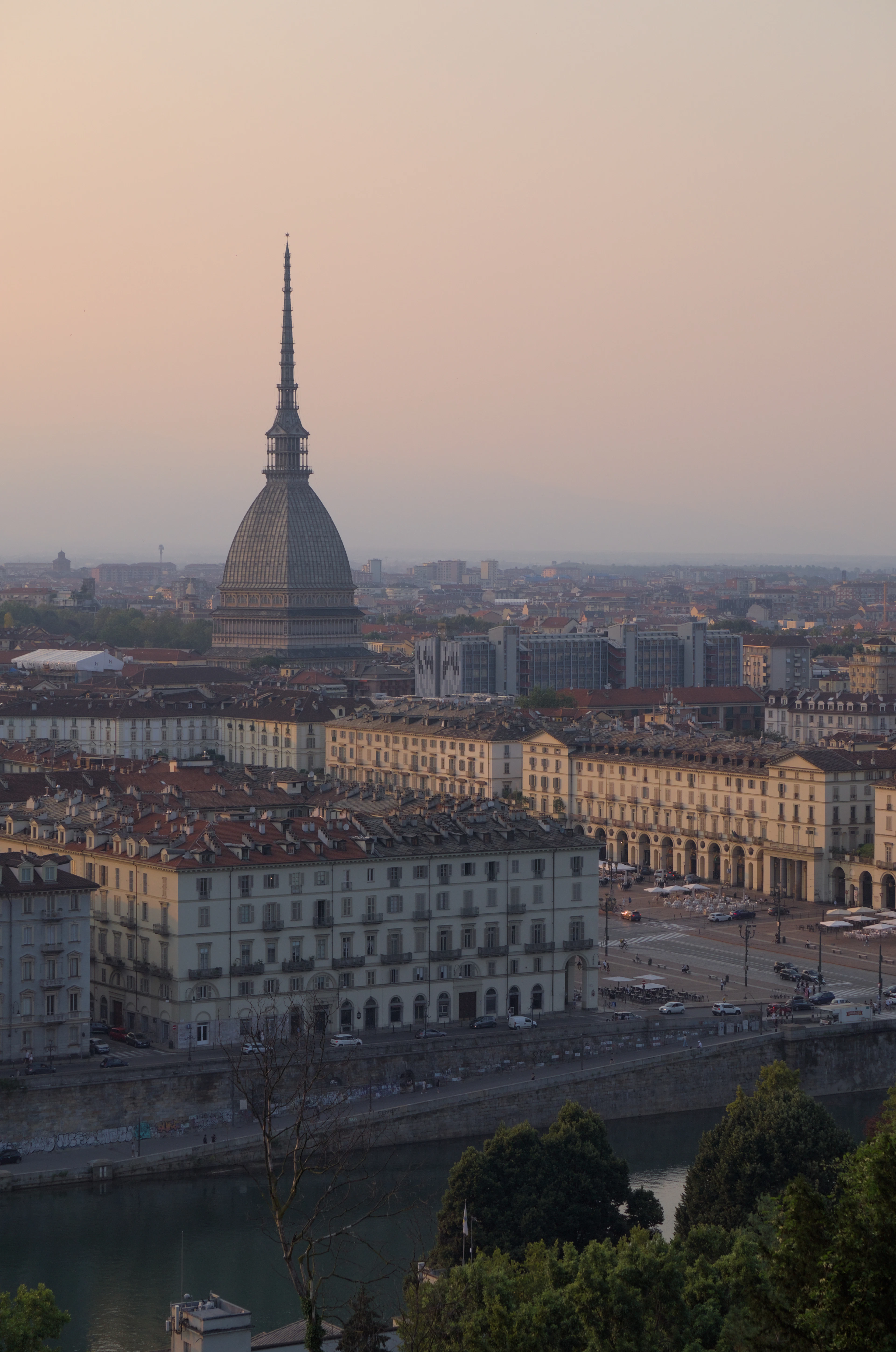 The domed spire of the Mole Antonelliana rising over Turin at sunset, above the long arcaded palazzi of Piazza Vittorio Veneto and the River Po