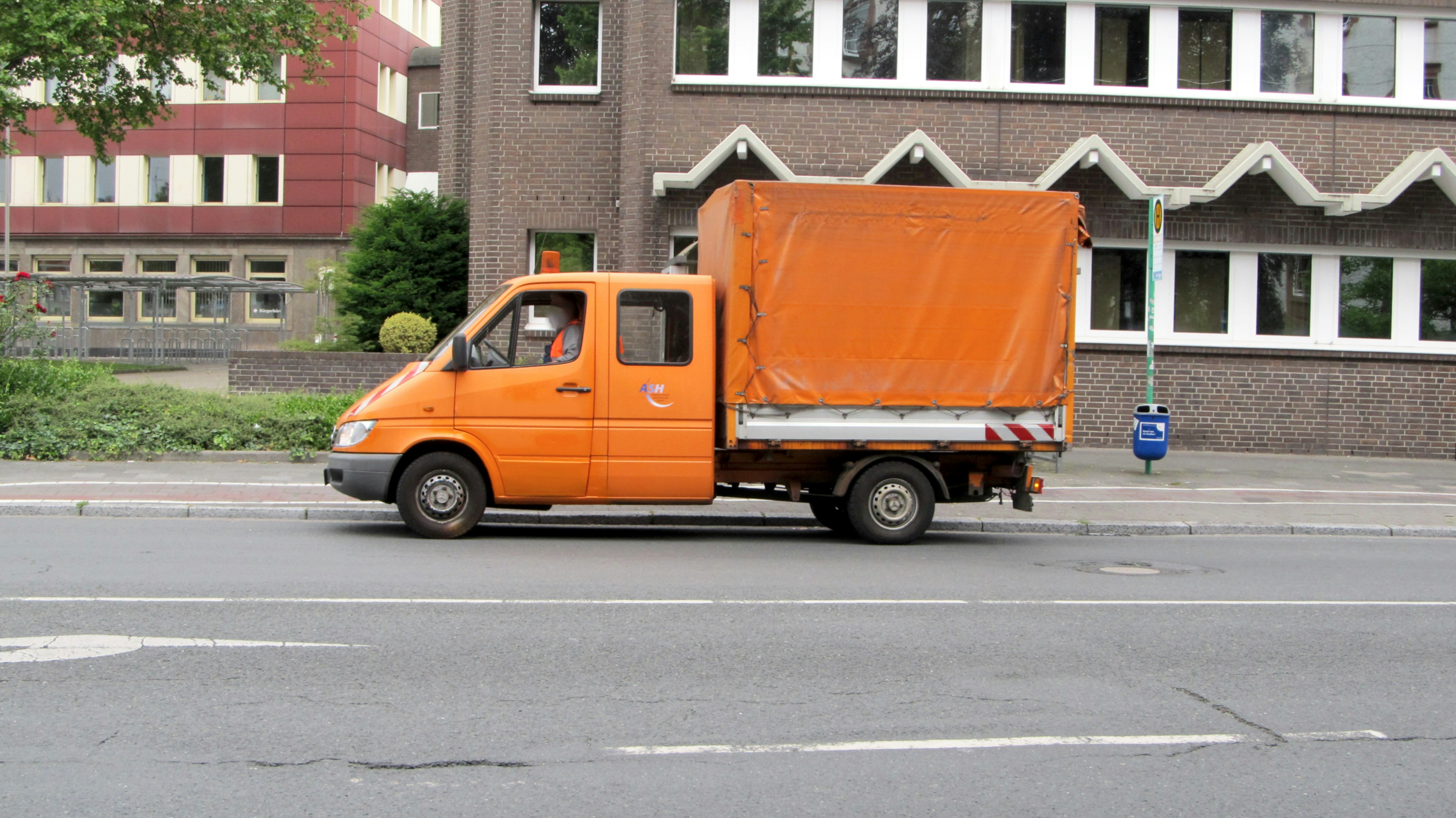 An orange truck driving down a street next to a tall building