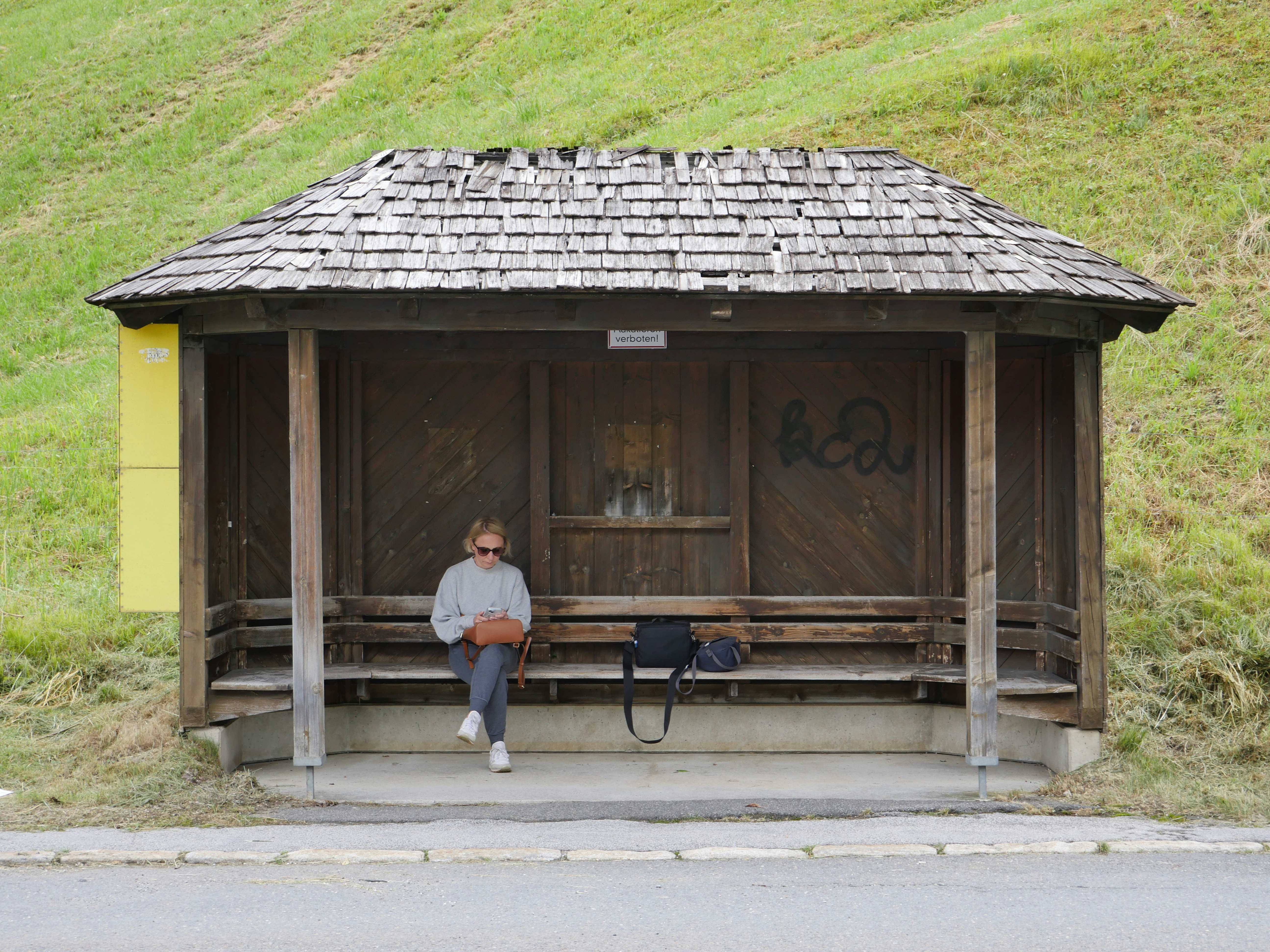A person sitting on a bench in front of a wooden shelter photo – Free ...