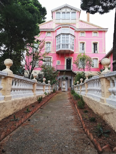 A pink house with a white fence and trees
