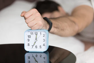 A man laying in bed with a clock on top of him