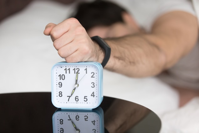 A man laying in bed with a clock on top of him