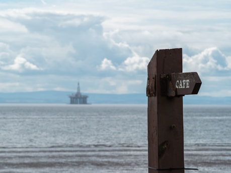 A wooden sign sitting on top of a beach next to the ocean