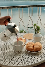A person pouring tea on a table with a view of the ocean