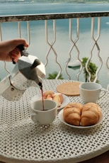 A person pouring tea on a table with a view of the ocean