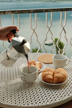 A person pouring tea on a table with a view of the ocean