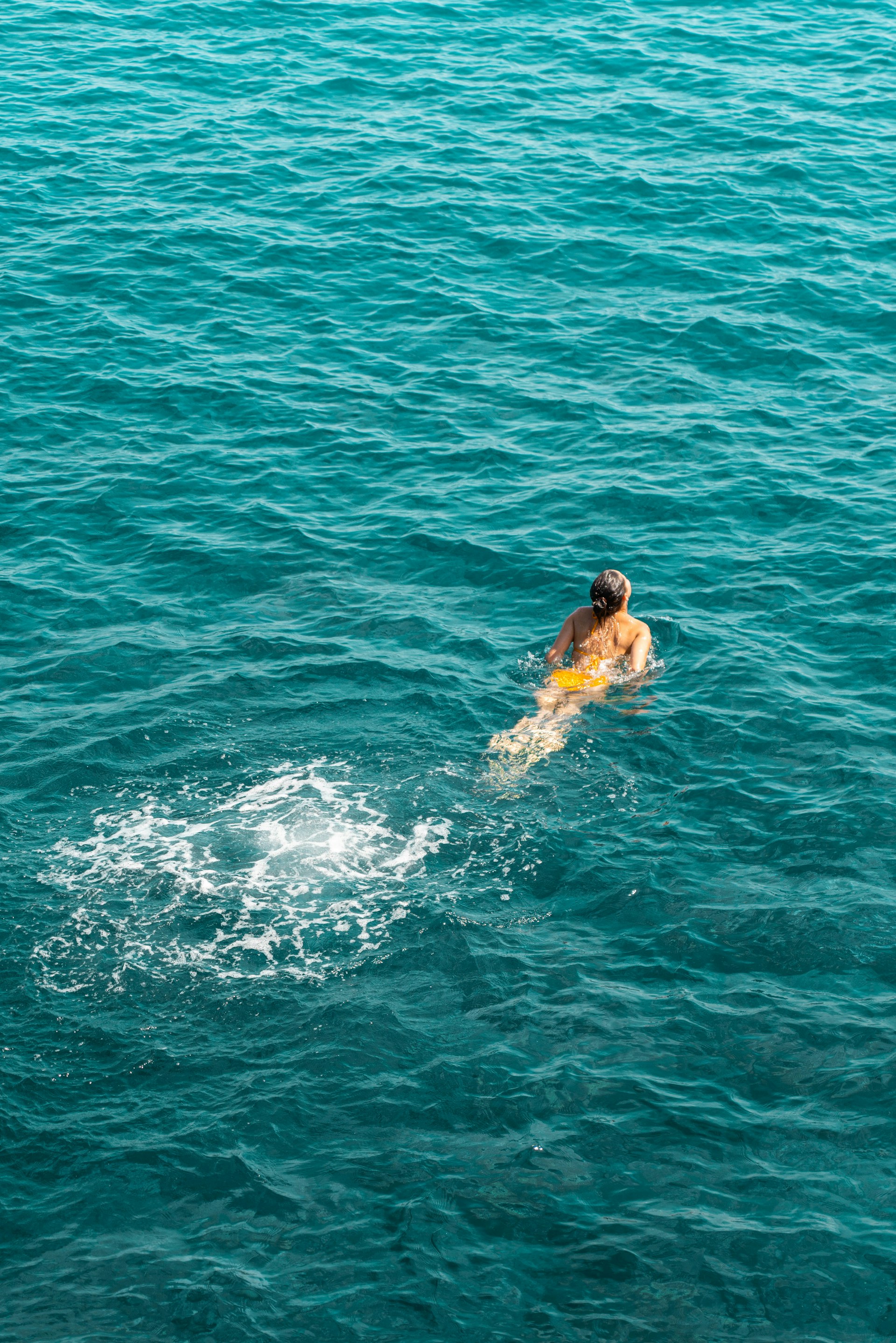 A man swimming in the ocean with a surfboard