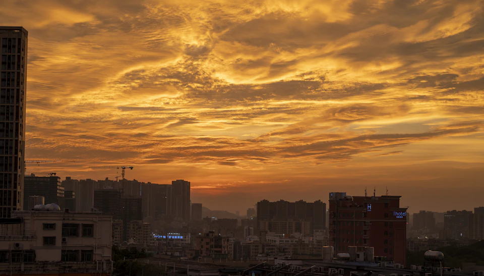 Vibrant cityscape at sunset with orange and yellow hues, sun setting behind skyscrapers
