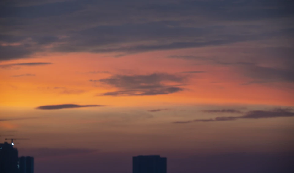 City skyline at sunset with orange and pink hues, sun setting behind buildings