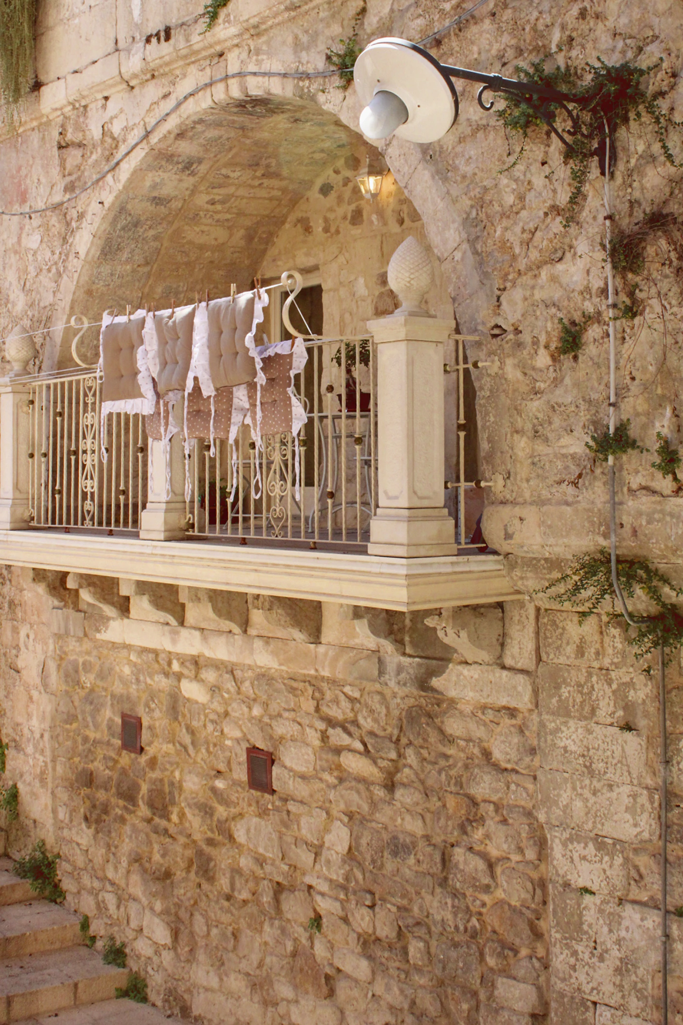 A stone balcony with ornate Baroque iron railings in Ragusa Sicily with warm golden limestone walls and deep blue sky above and the layered rooftops of the historic city visible below