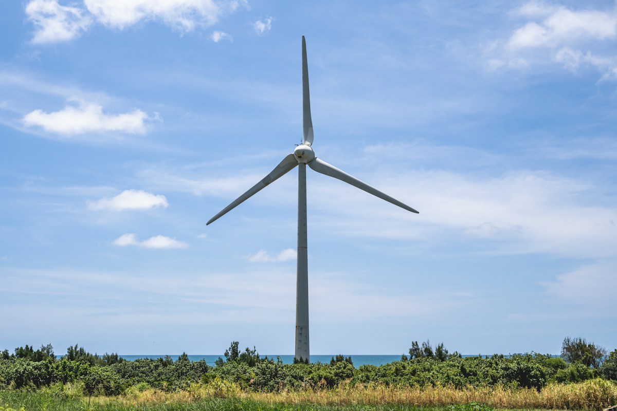 A white wind turbine among the fields near the coast in Houlong, Miaoli, under a blue sky