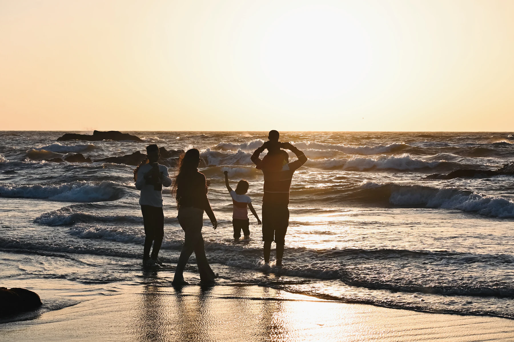Family standing in the waves at sunset