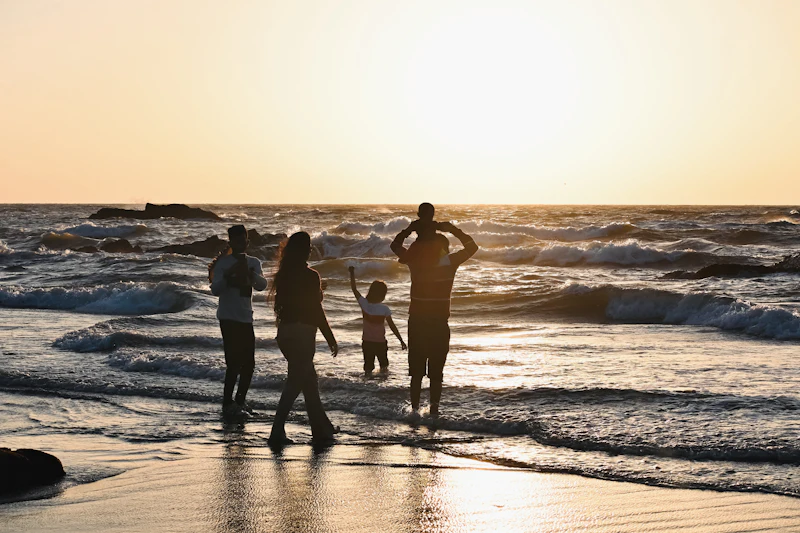Family standing in the waves at sunset