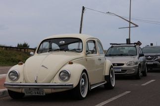 A white vw bug driving down a street next to other cars
