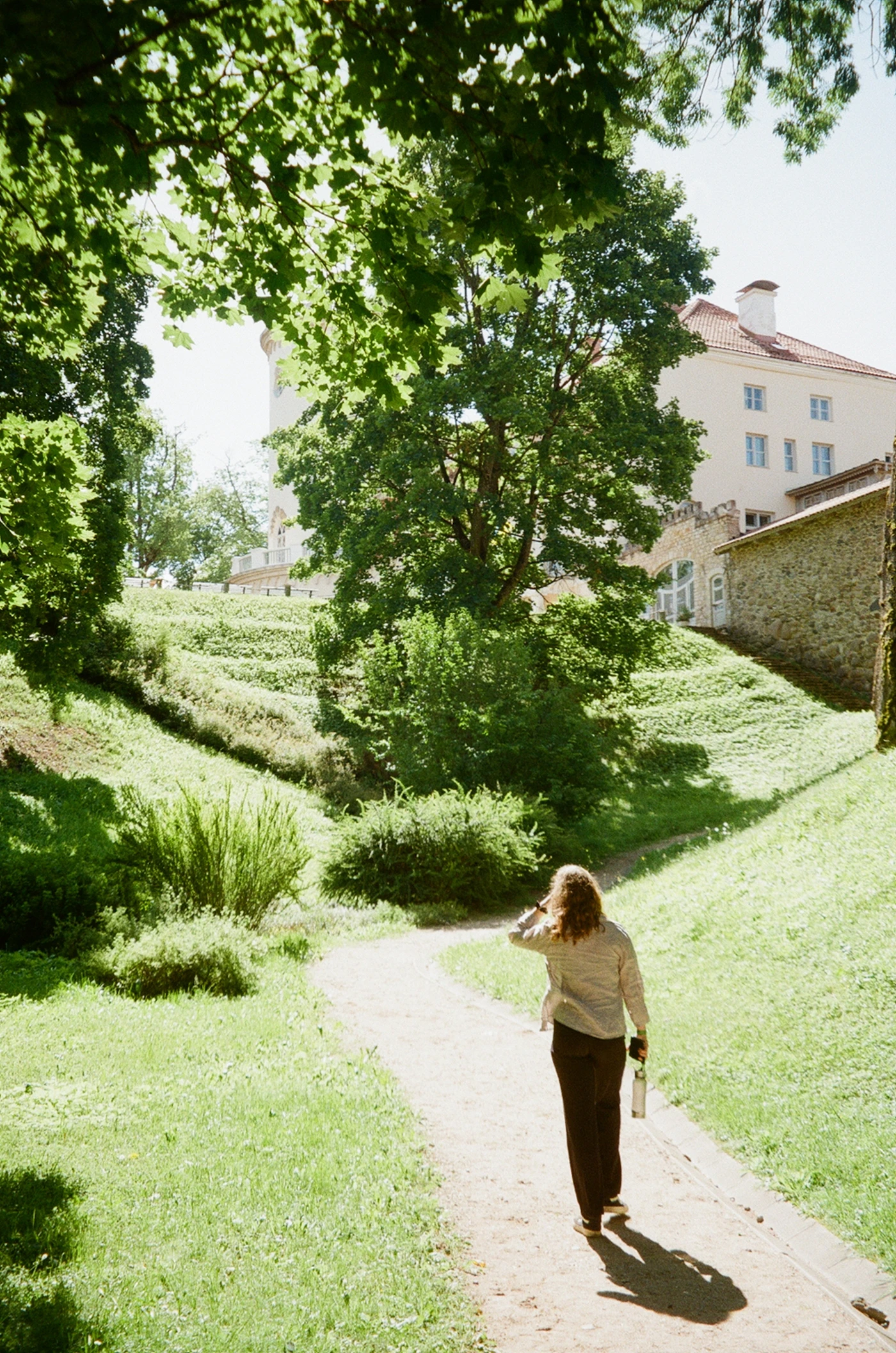A woman walking along a sunlit path in a park.