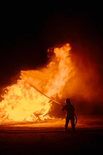 A man holding a fire hose in front of a large fire