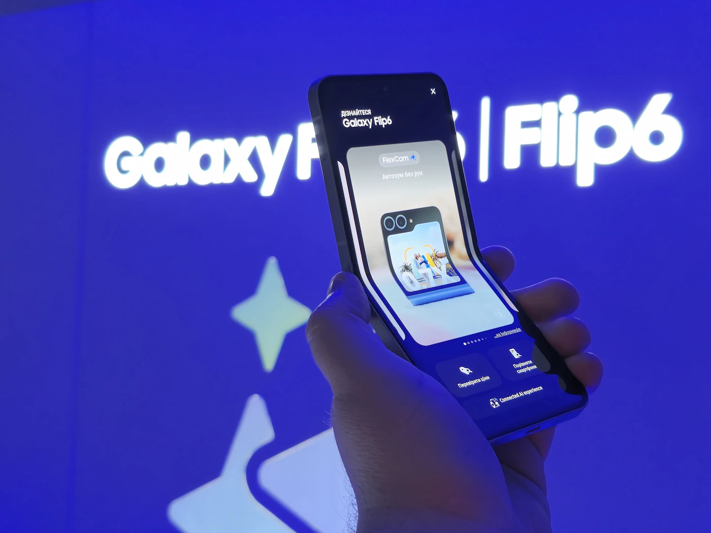 A hand holds a Galaxy Z Flip6 in front of an illuminated Galaxy Flip6 sign