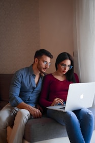 A man and woman sitting on a couch looking at a laptop