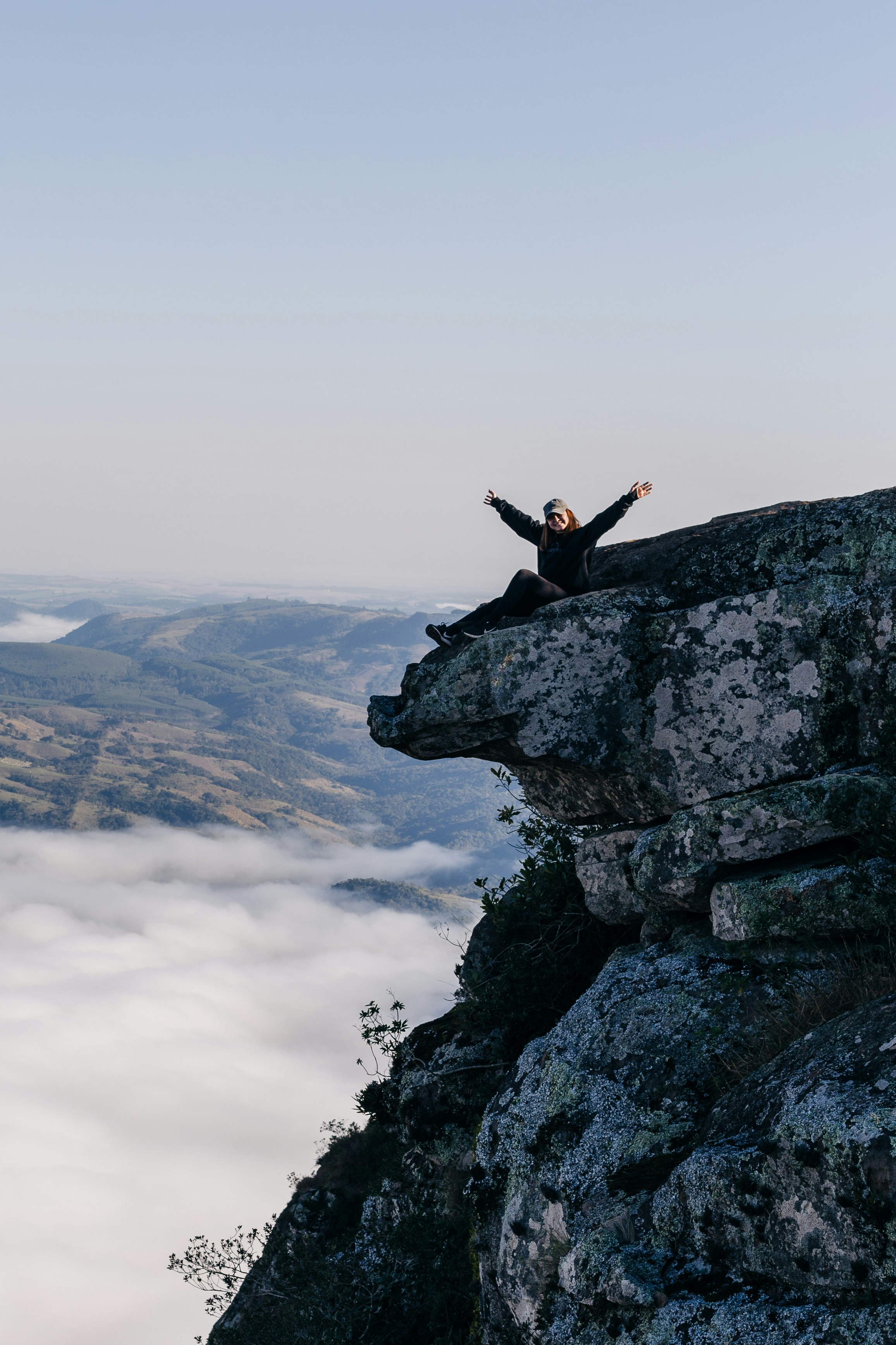 A person sitting on top of a cliff above the clouds