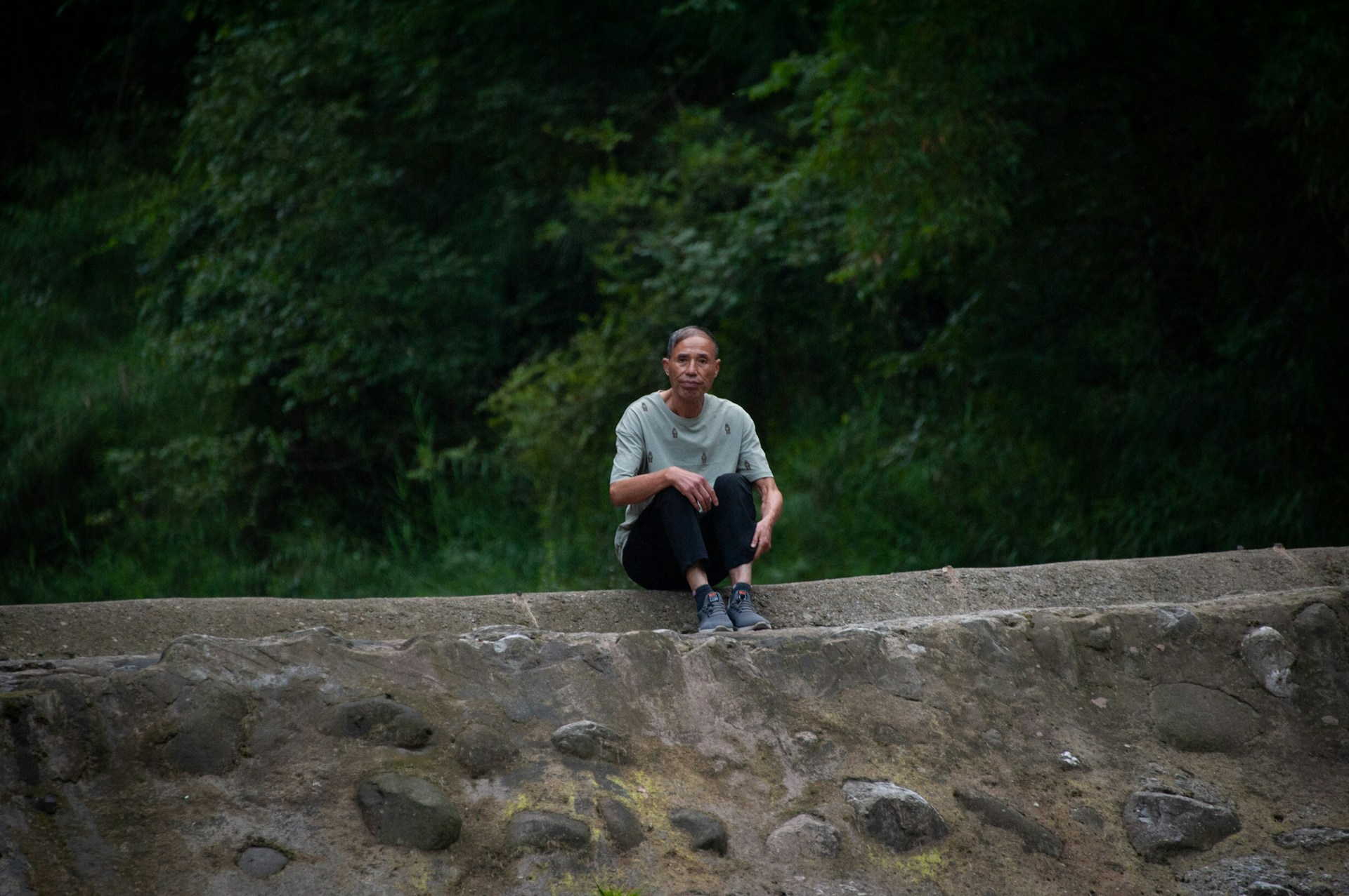 A woman sitting on a rock wall next to a forest