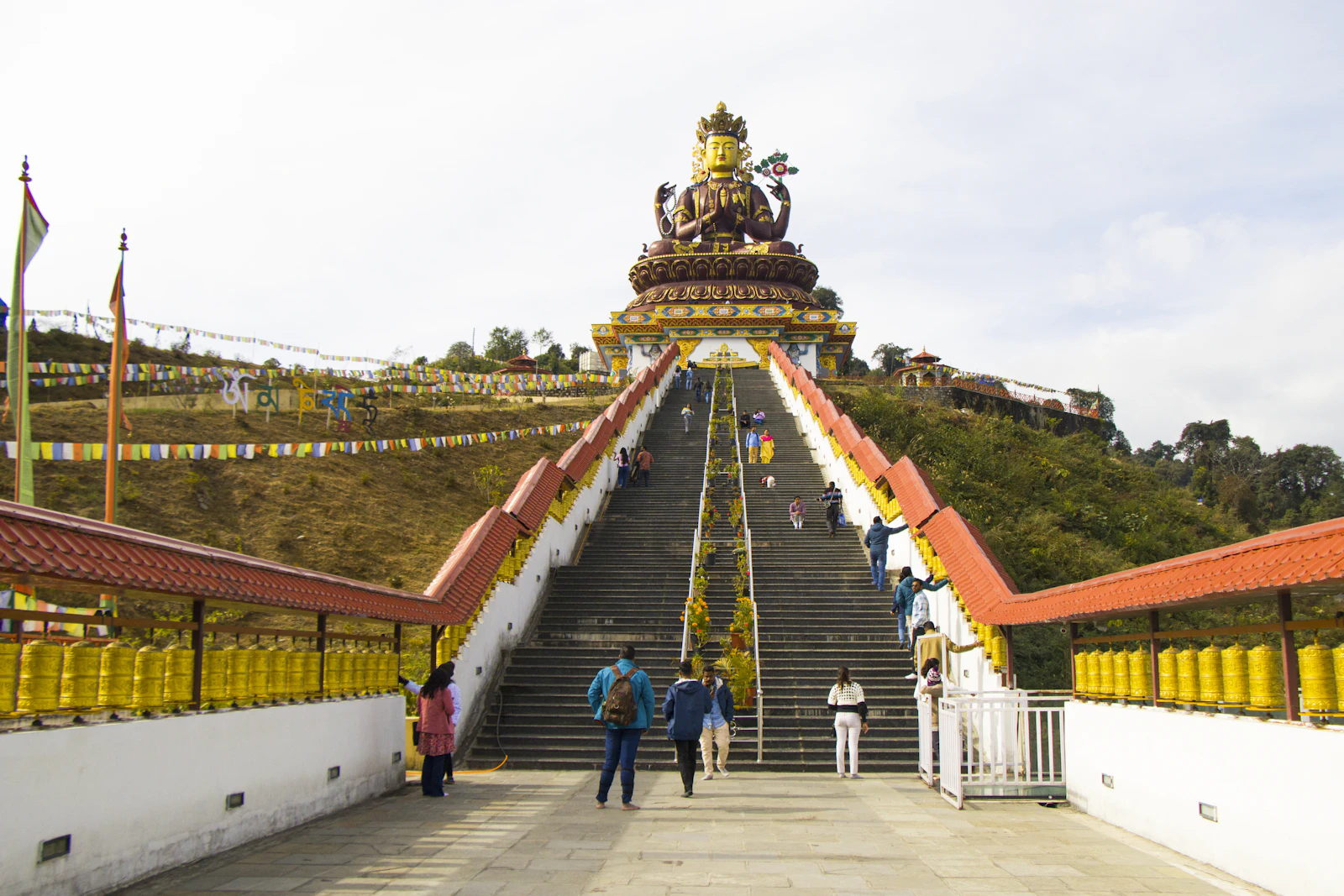 Visitors on the walkway lined with golden prayer wheels leading up the steps to the Chenrezig statue at Pelling