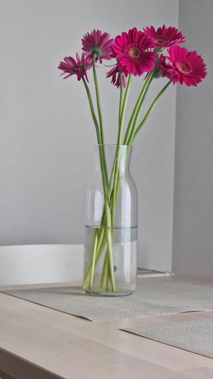 A clear glass vase of soft pink garden flowers arranged on a table