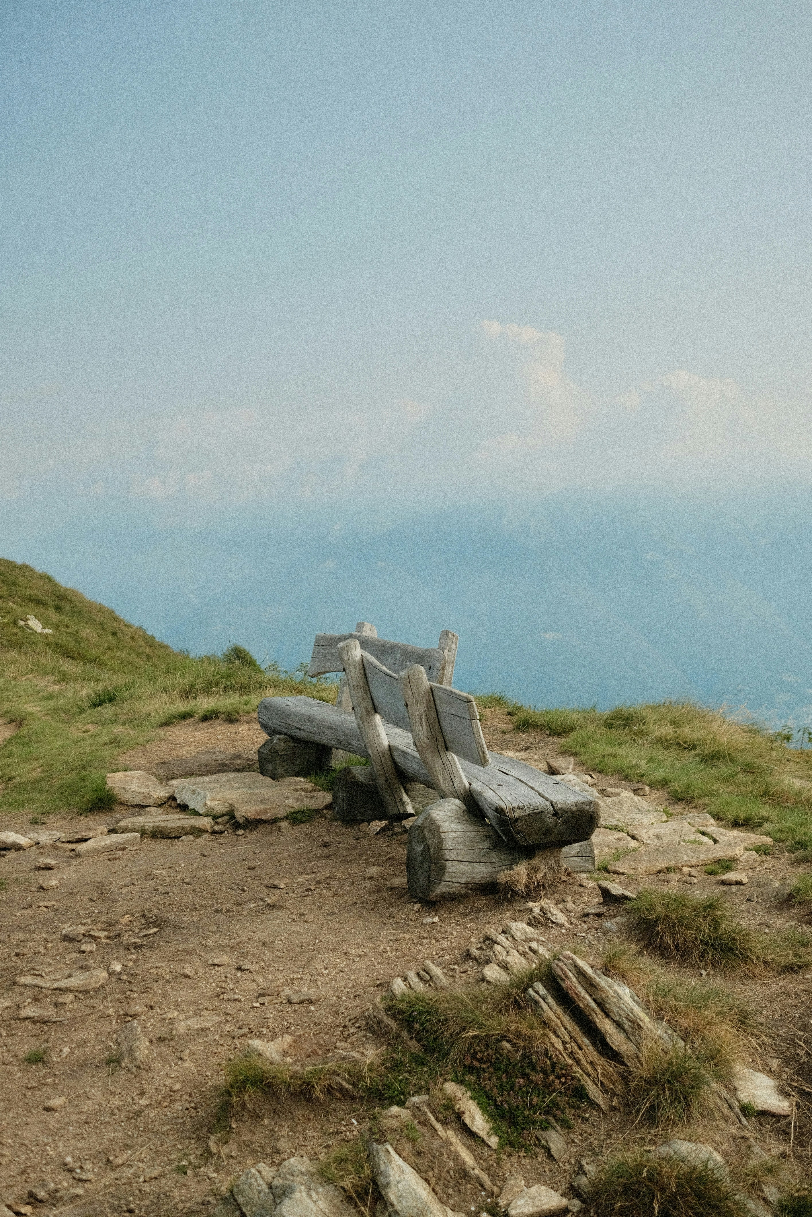 A wooden bench sitting on top of a grass covered hillside