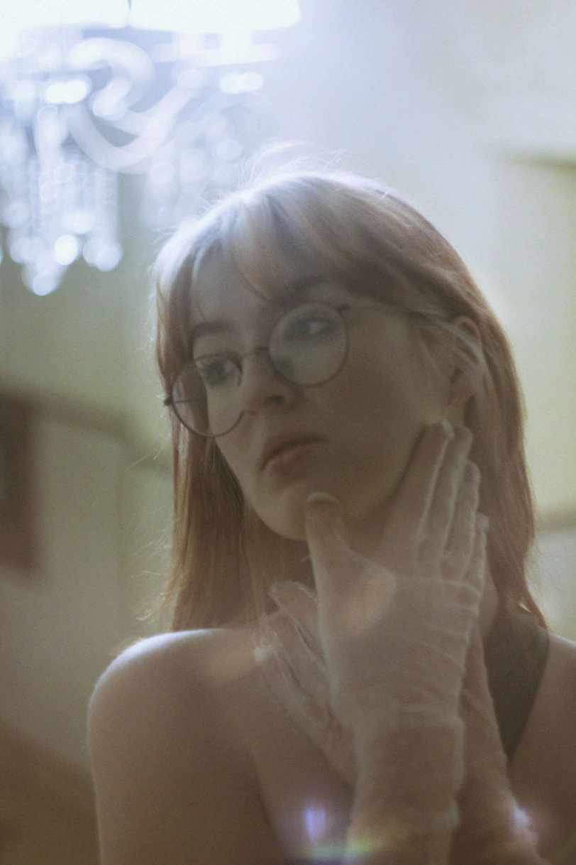 A woman with glasses is looking in the mirror