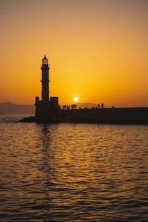 The sun is setting behind a lighthouse on the water