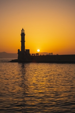 The sun is setting behind a lighthouse on the water