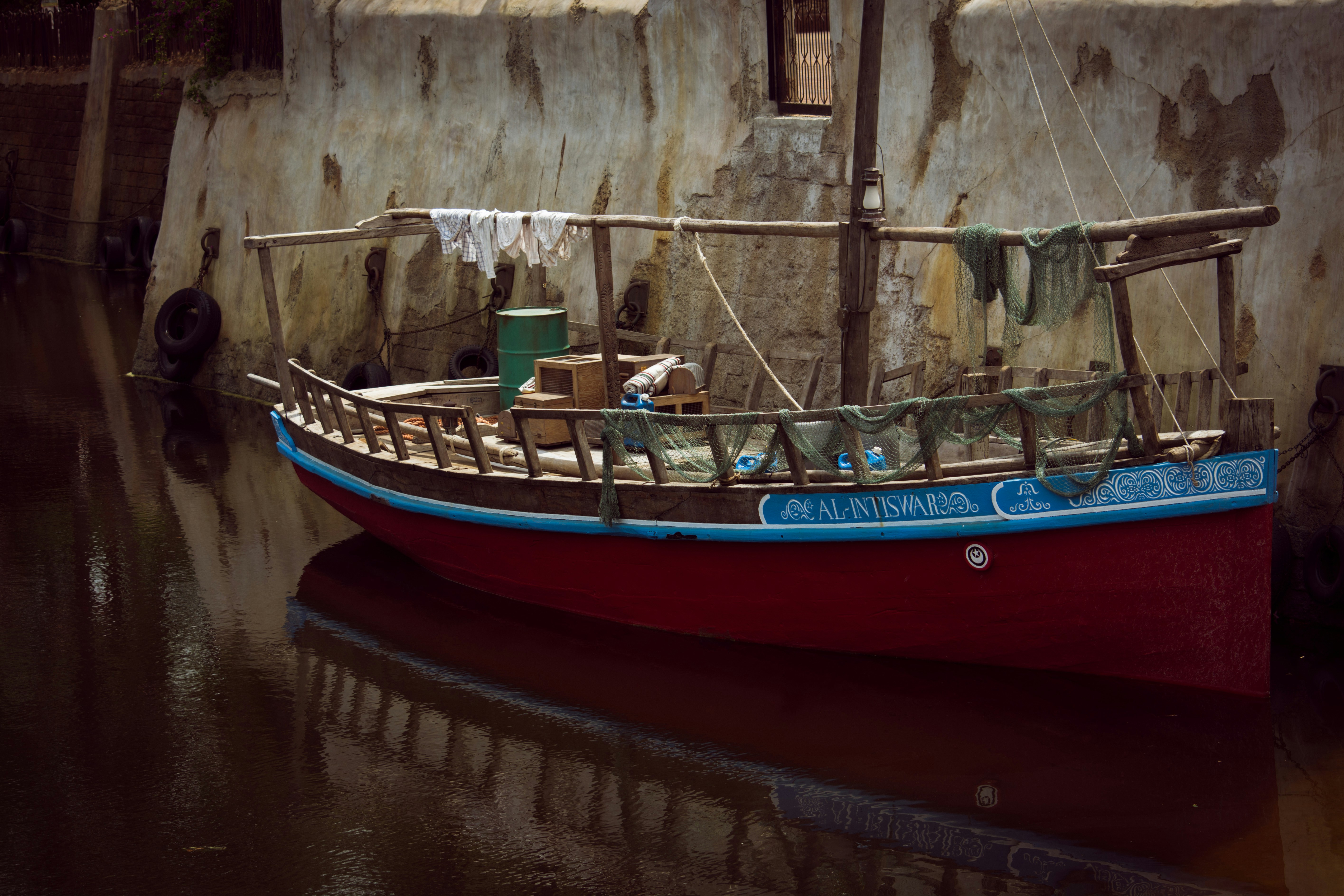 A red and blue boat in a body of water, Wooden boat stationed on the port.