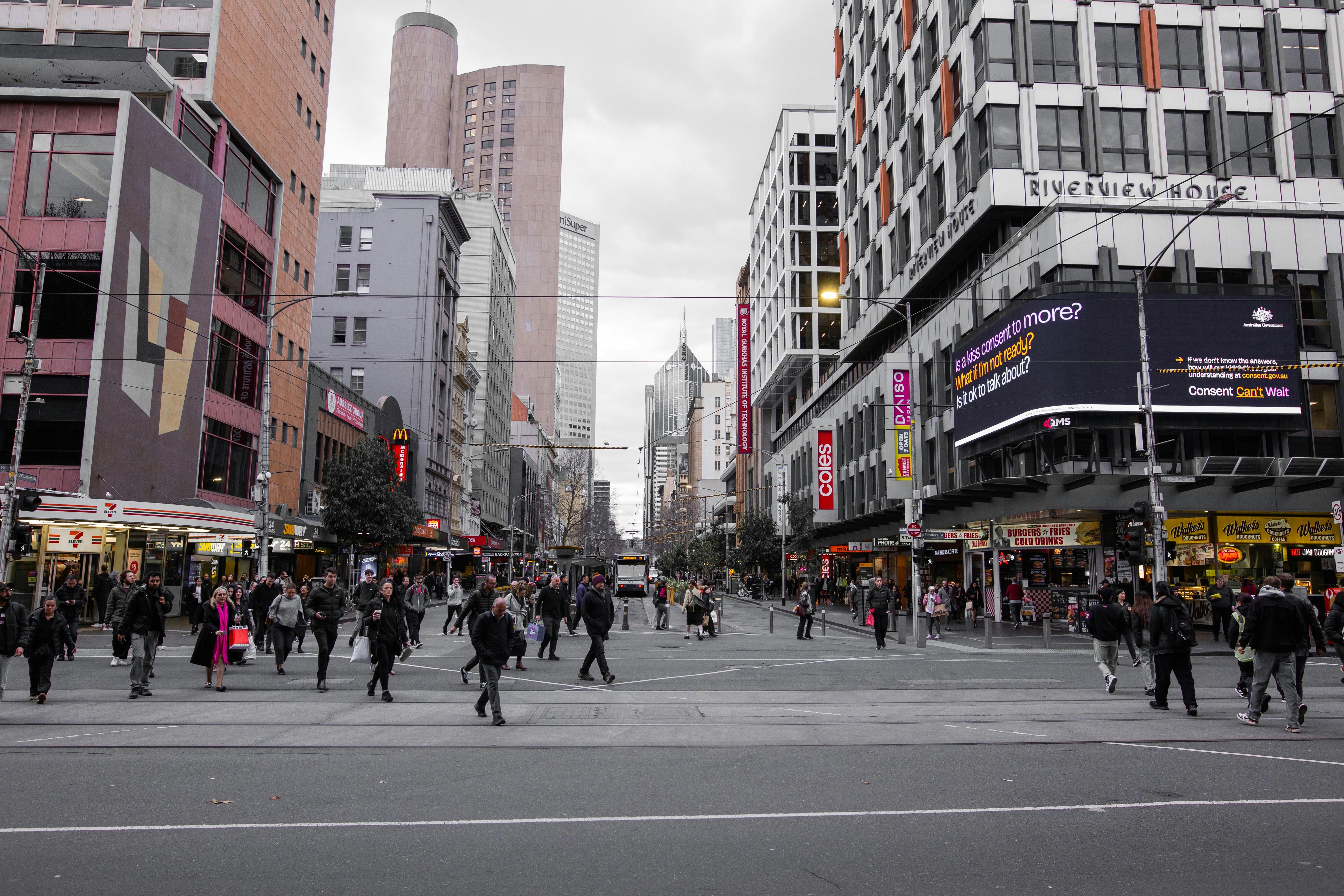 A crowd of people walking across a street next to tall buildings