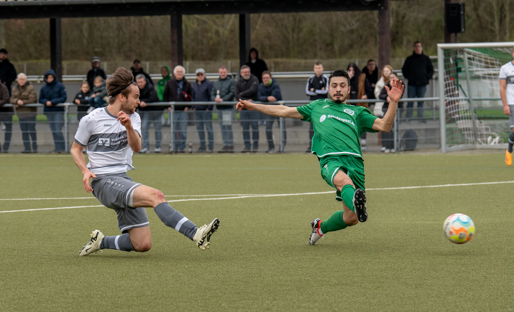 A slide tackle in an amateur match with spectators along the rail
