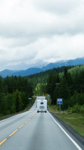 A white truck driving down a road next to a forest