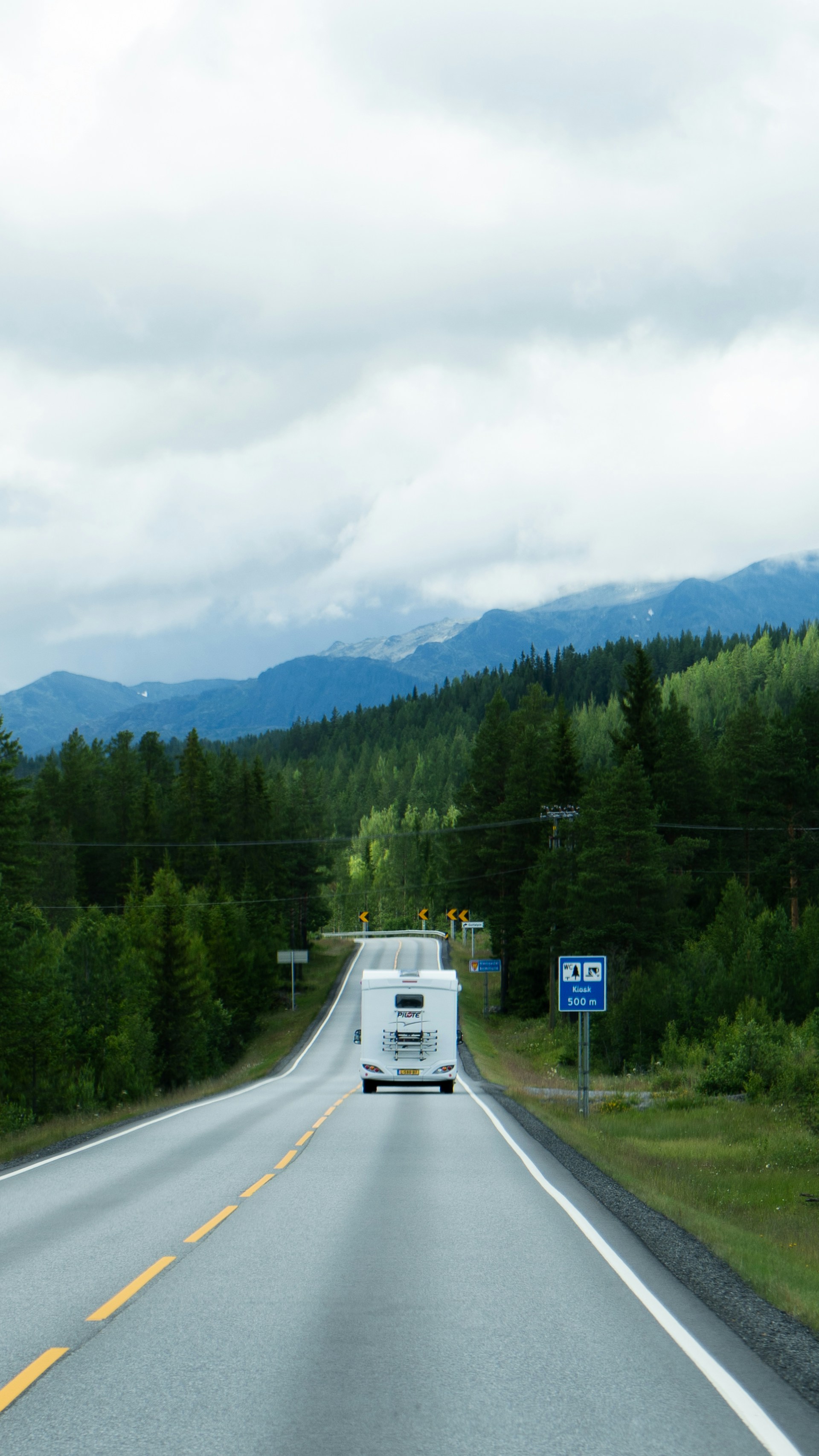A white truck driving down a road next to a forest