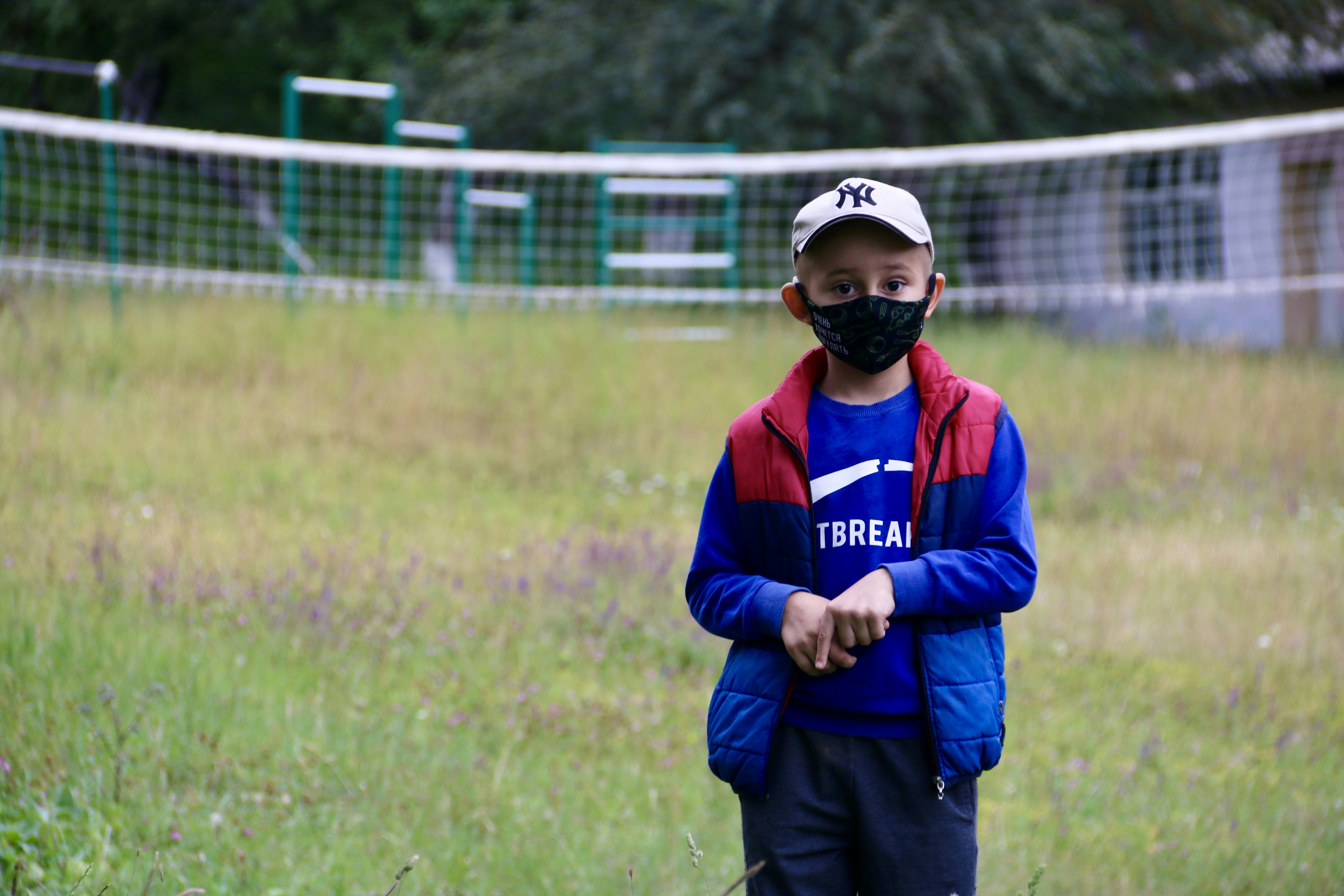 A young boy wearing a face mask standing in a field