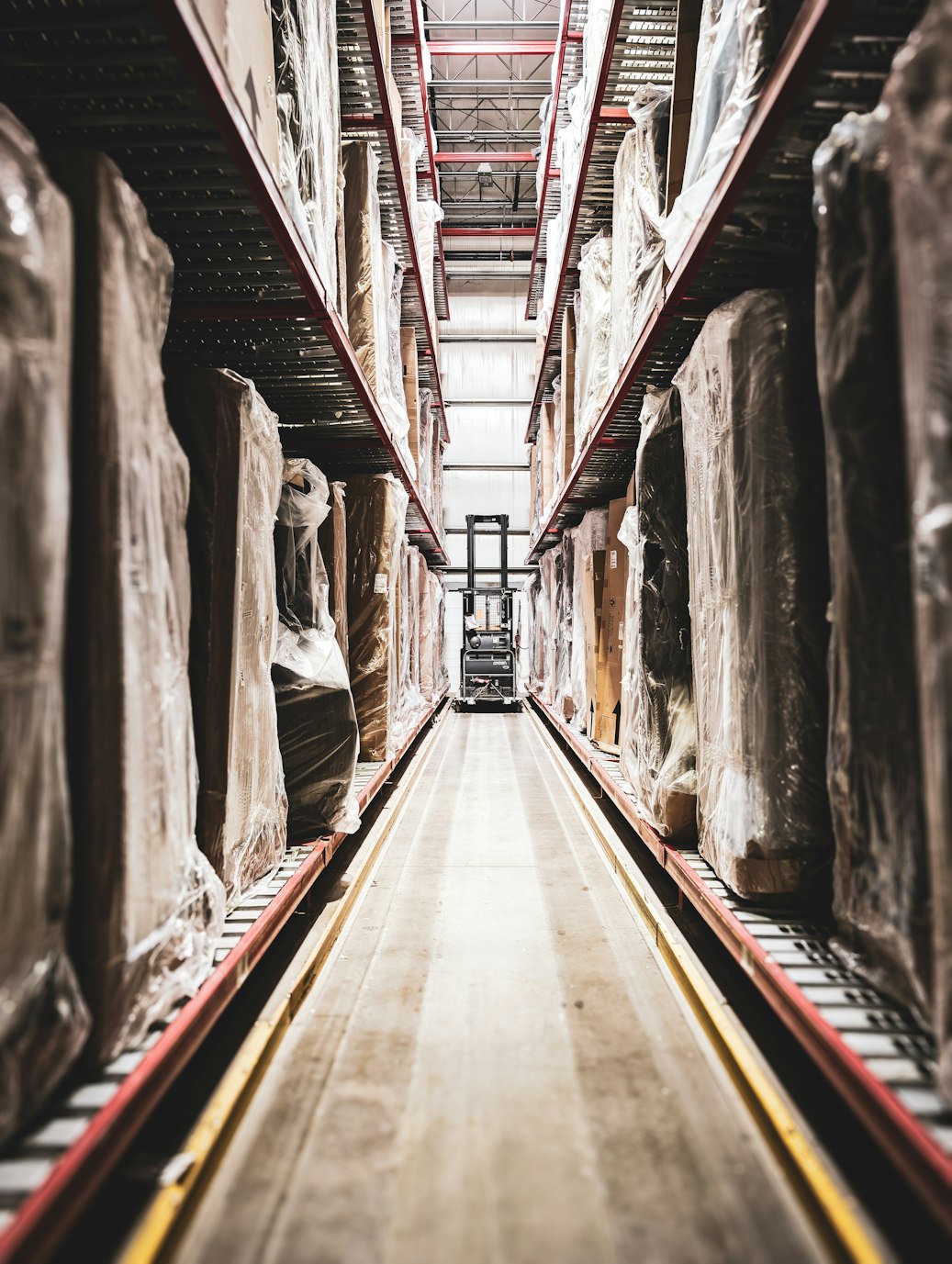Long warehouse aisle with tall shelving units filled with wrapped rectangular packages
