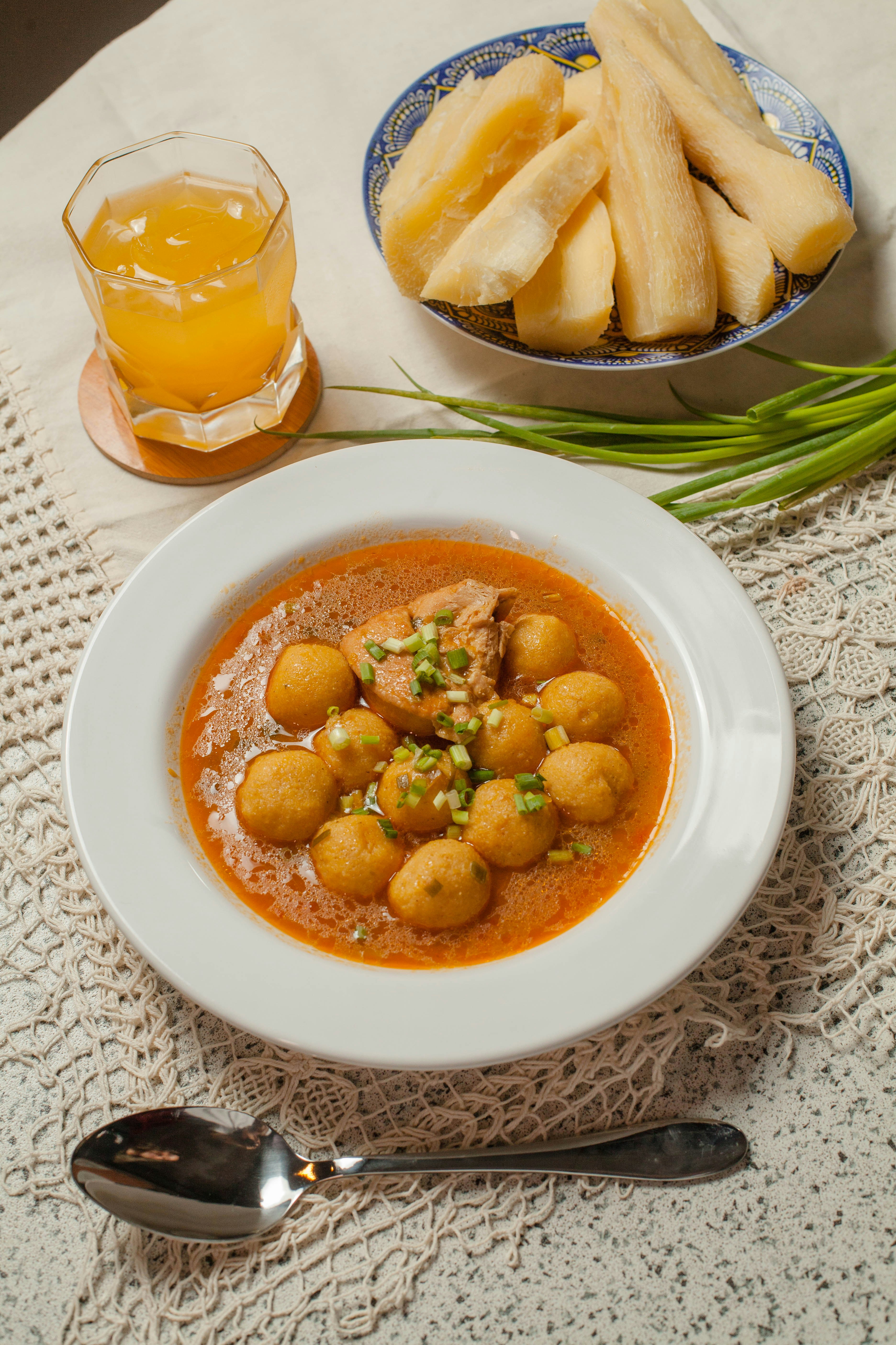 A bowl of soup next to a bowl of bread and a glass of orange juice