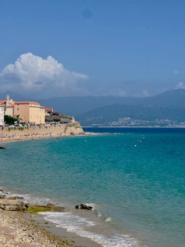 Die Zitadelle von Ajaccio und die alten Stadtmauern, gesehen von der Bucht, mit türkisfarbenem Mittelmeerwasser im Vordergrund und korsischen Bergen im Hintergrund