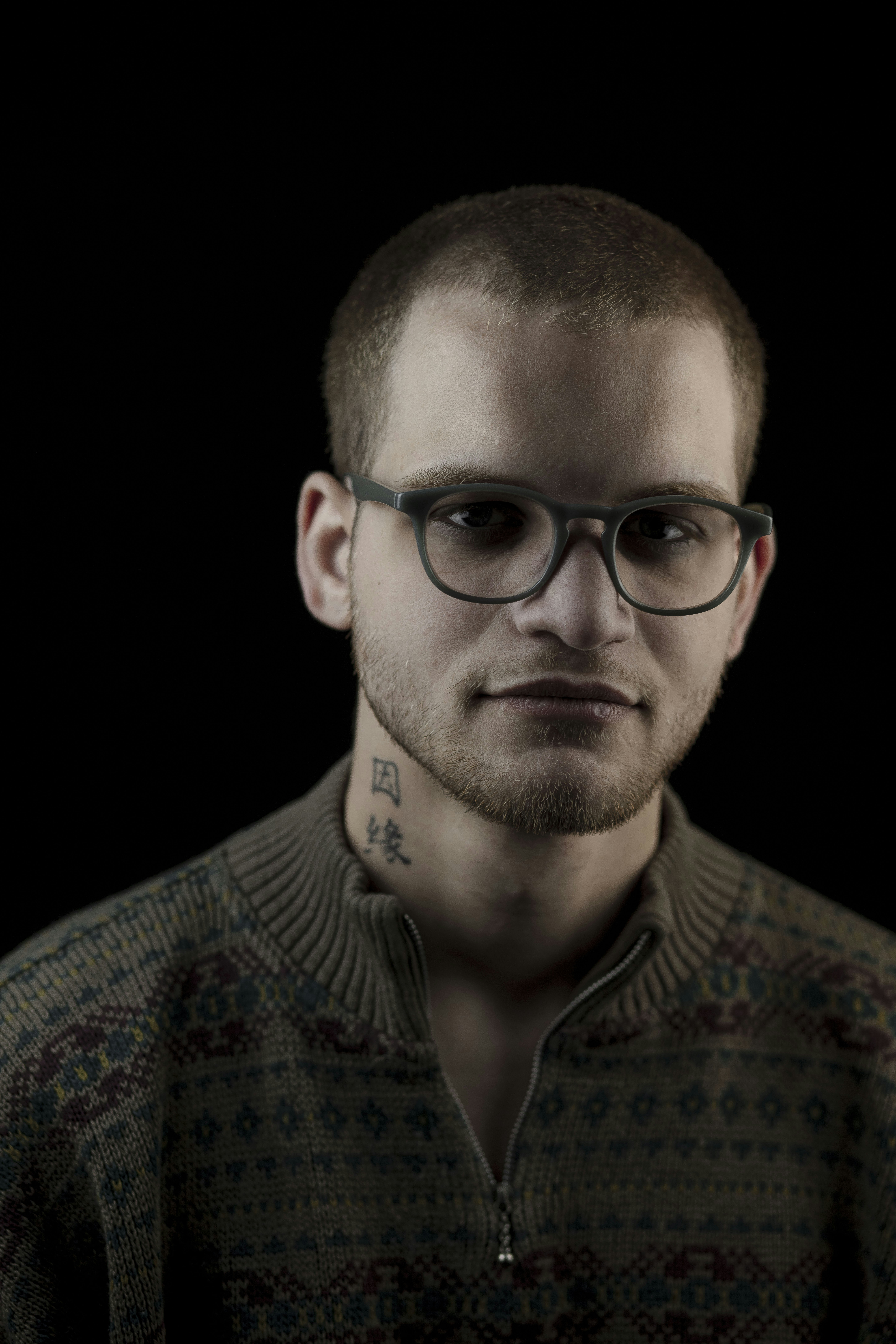 A man wearing glasses and a sweater looks at the camera