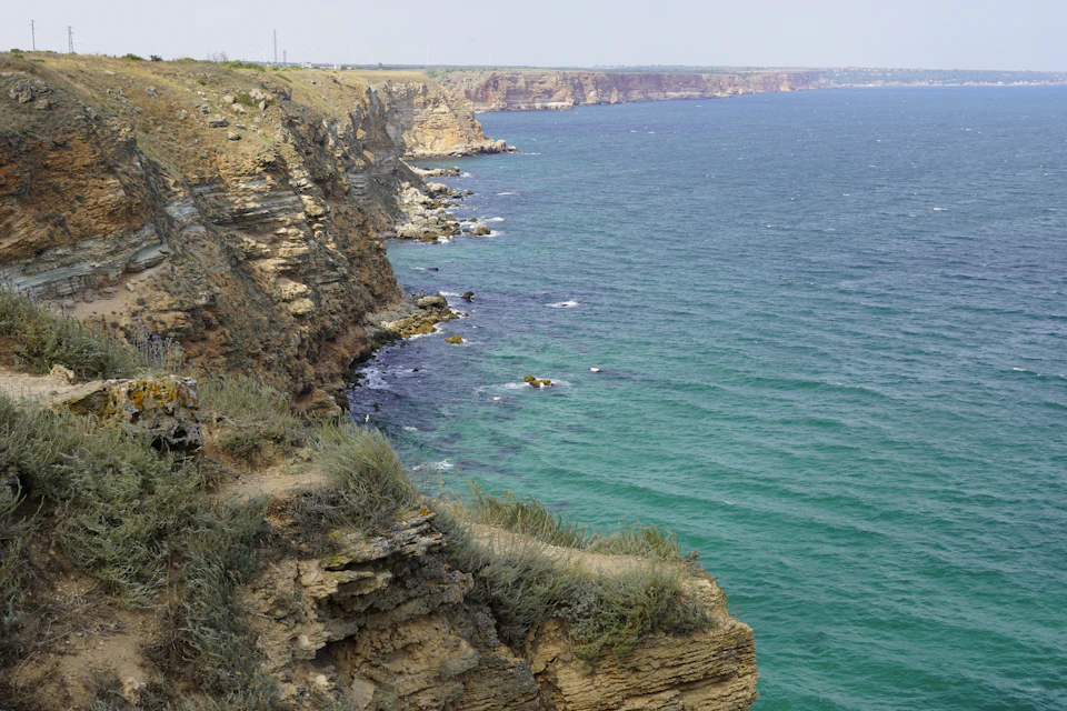 Cliffside overlooking deep blue ocean with white waves crashing against its base