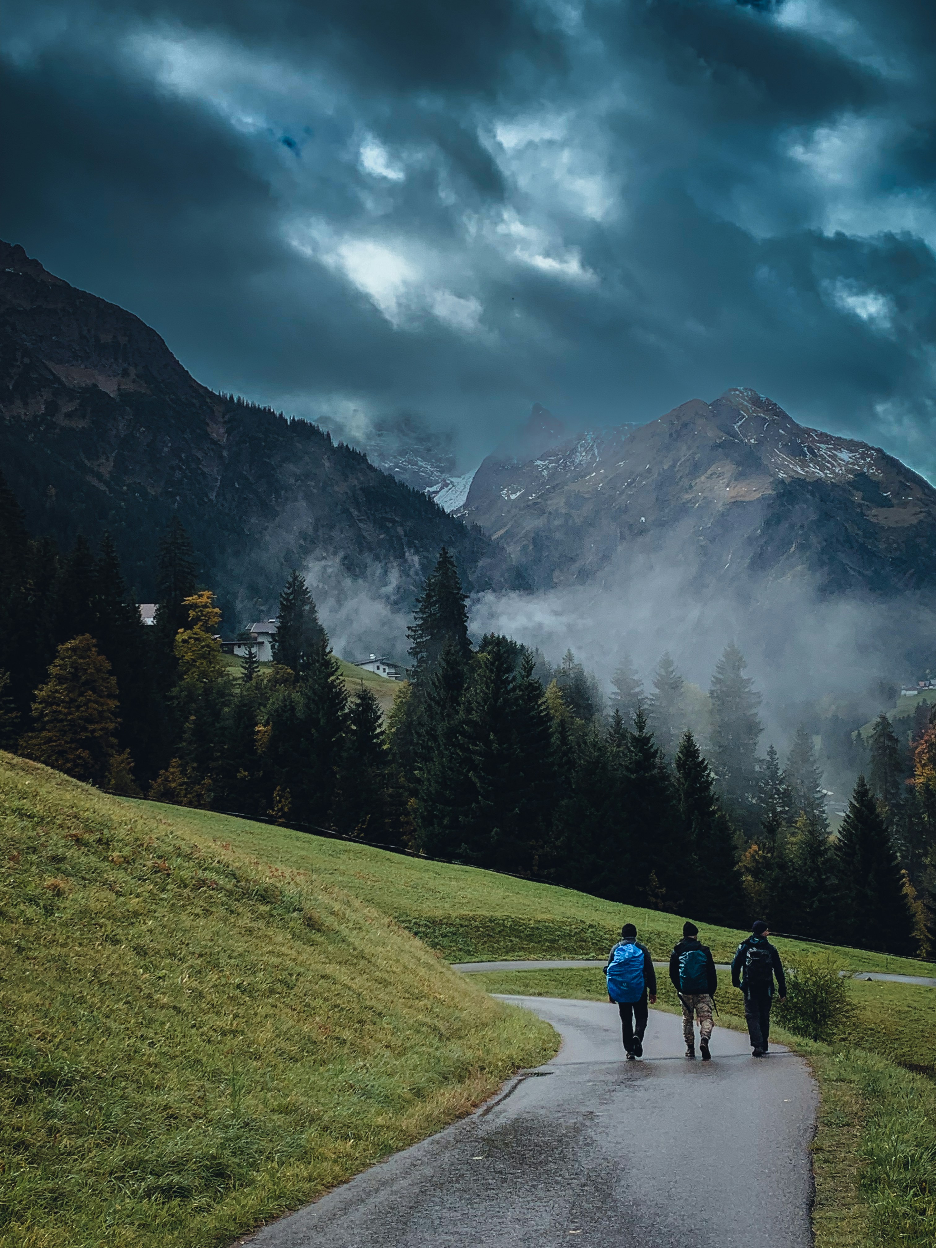 Three people walking down a road in the mountains